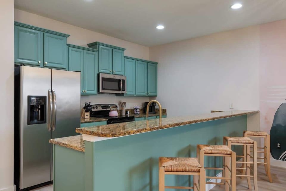 Modern kitchen with stainless steel appliances, vibrant teal cabinets, and granite countertops. Ideal for cooking and casual dining with cozy bar seating. Experience style and comfort—book your stay today!
