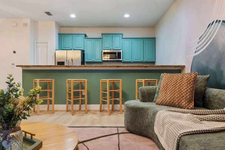 Spacious open-plan living area with modern teal kitchen, cozy bar seating, and plush lounge. Perfect for relaxation and entertaining. Enjoy comfort and style—book your stay today!