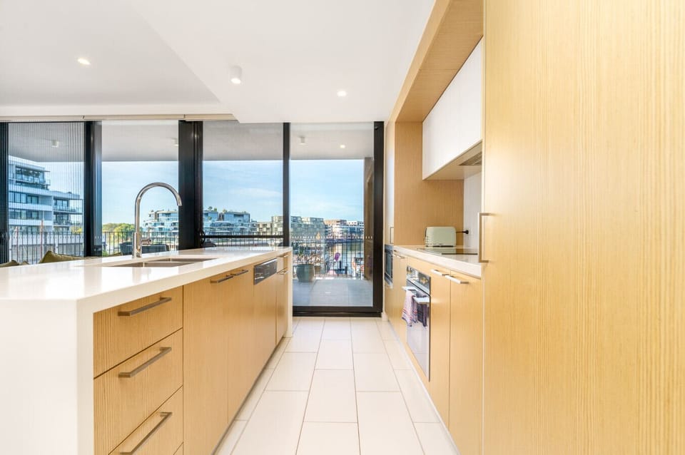 A modern open kitchen with light wood cabinets, a spacious white countertop, and a complete set of appliances and utensils for preparing meals.