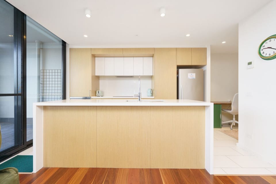 A modern open kitchen with light wood cabinets, a spacious white countertop, and a complete set of appliances and utensils for preparing meals.