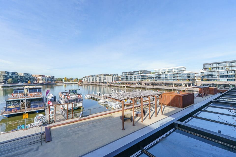 A scenic view of the marina with boats docked along the calm lake, surrounded by modern apartments and the lively atmosphere of Kingston Foreshore.