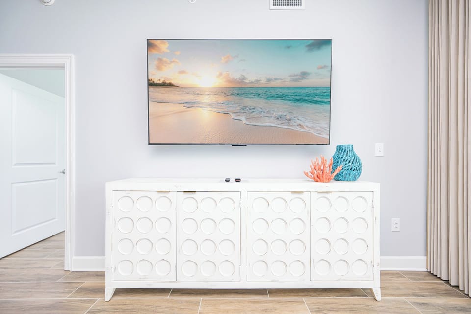 Enjoy the large TV above a stylish white cabinet, complemented by colorful decor and inviting textures in the living area