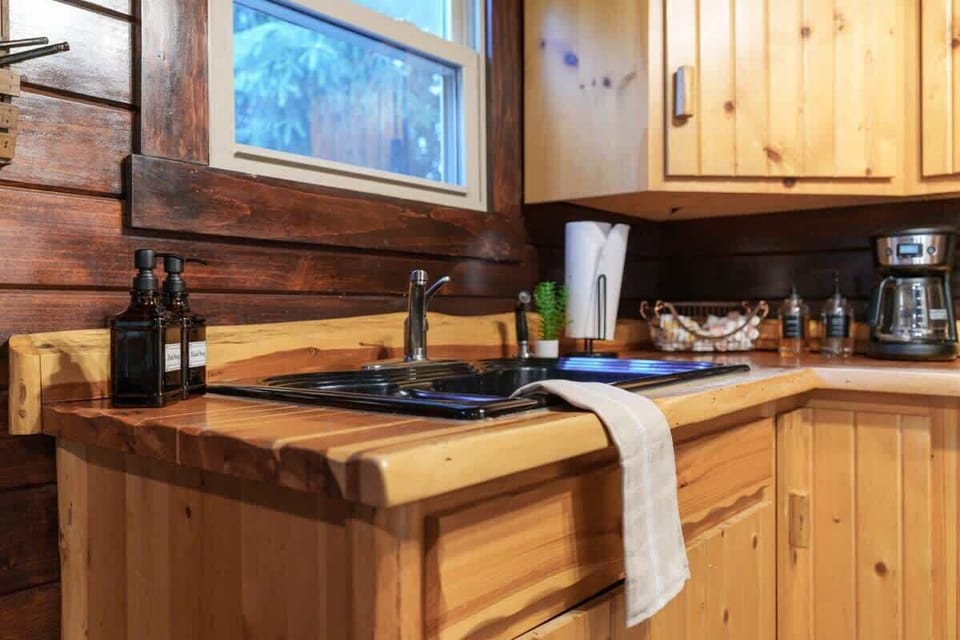 Close-up of the cozy cabin kitchen sink area w/ warm wood counters & forest-view window
