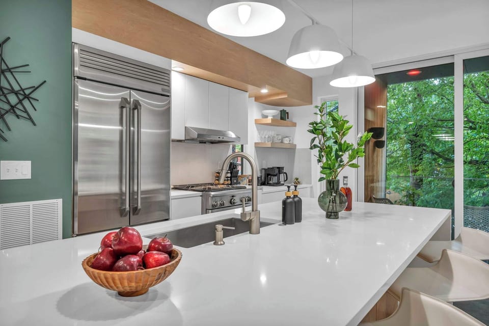 This modern kitchen showcases stainless steel appliances, a spacious island with pendant lighting, and greenery, blending functionality with elegance.