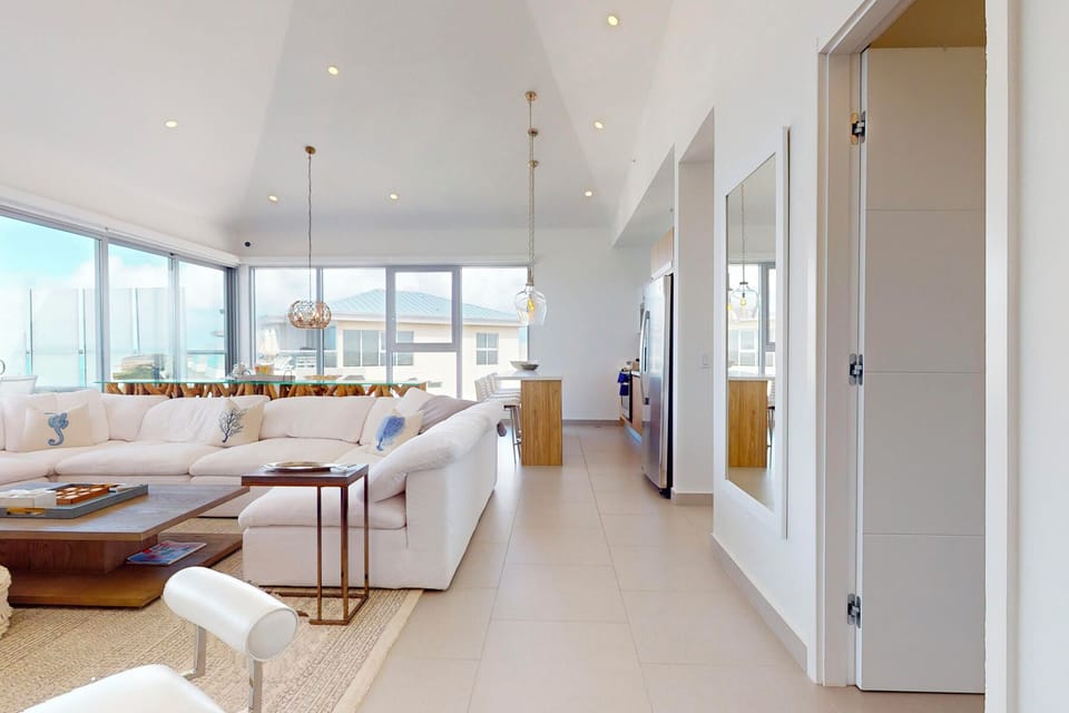 Sink into your comfortable sofa and enjoy ocean breezes flowing through floor-to-ceiling windows in this bright, open-plan living space with vaulted ceilings and coastal charm.