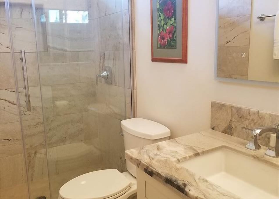 Enjoy a bright and elegant bathroom with glass shower, stone counters, and a pop of island inspired art.

