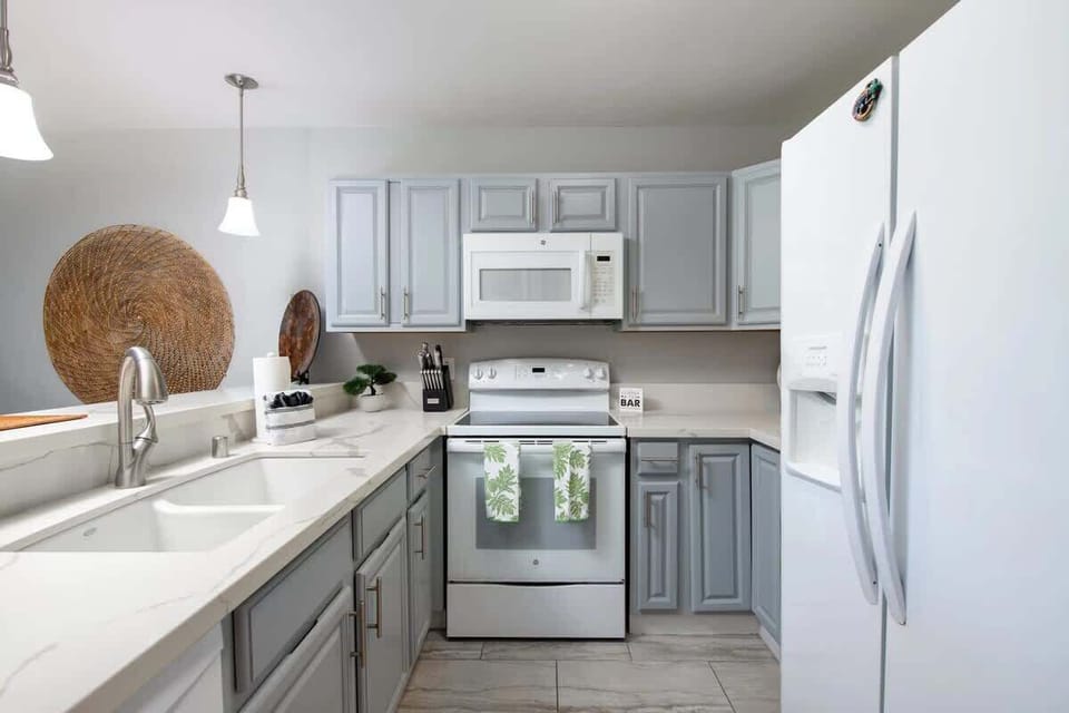 Chic kitchen with pale blue cabinets, white countertops, and full appliances including microwave.

