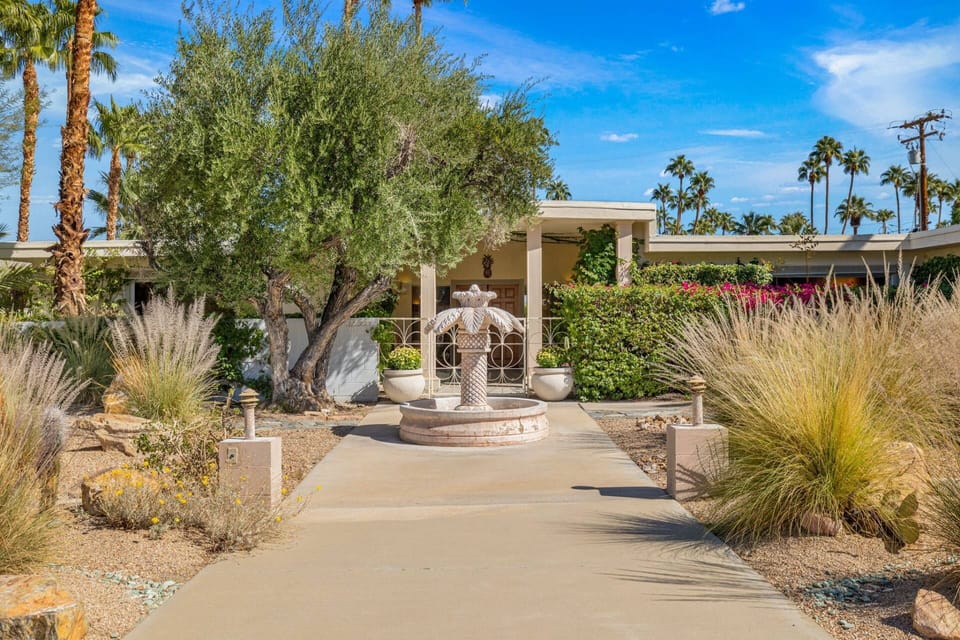 Charming desert oasis entry with lush landscaping and a classic fountain centerpiece.
