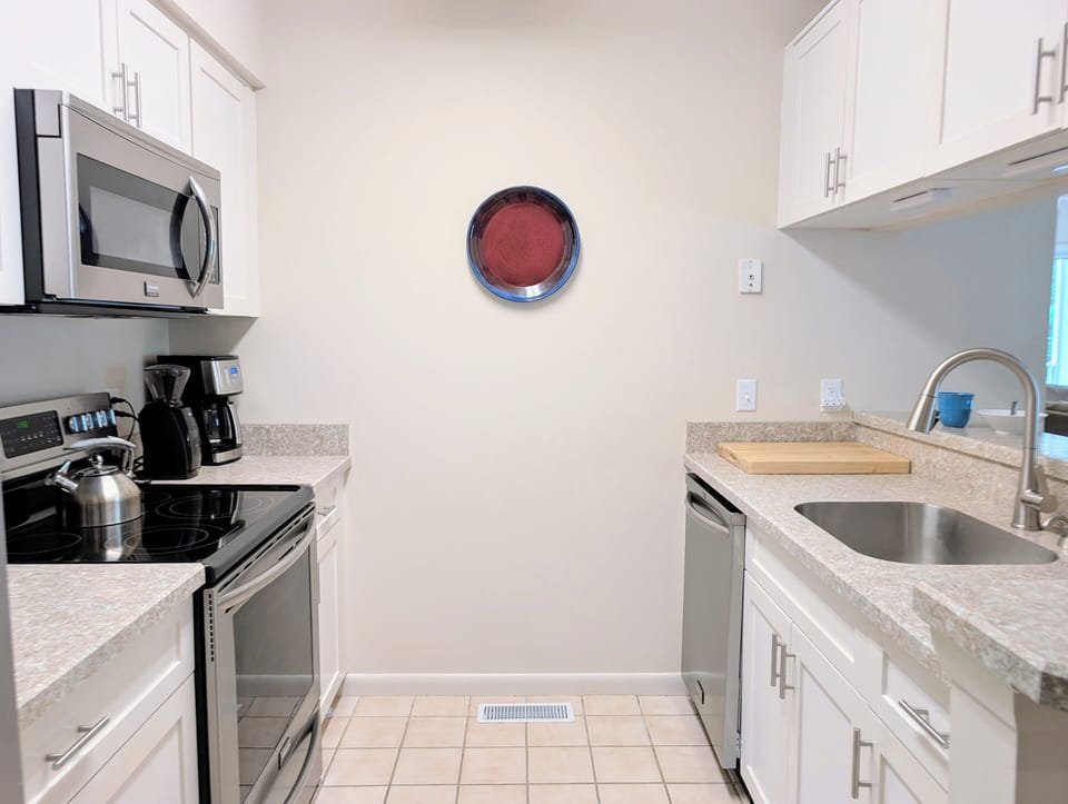 Modernized Gourmet Kitchen - This crisp white kitchen is fully equipped for the modern home cook, featuring premium stainless steel appliances, ample counter space, and a clean, minimalist aesthetic that keeps the space feeling bright and organized.