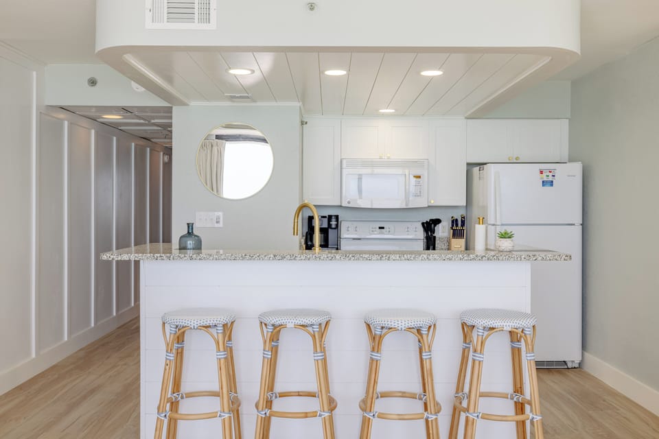 Modern kitchen with a granite countertop and four rattan bar stools for casual dining.