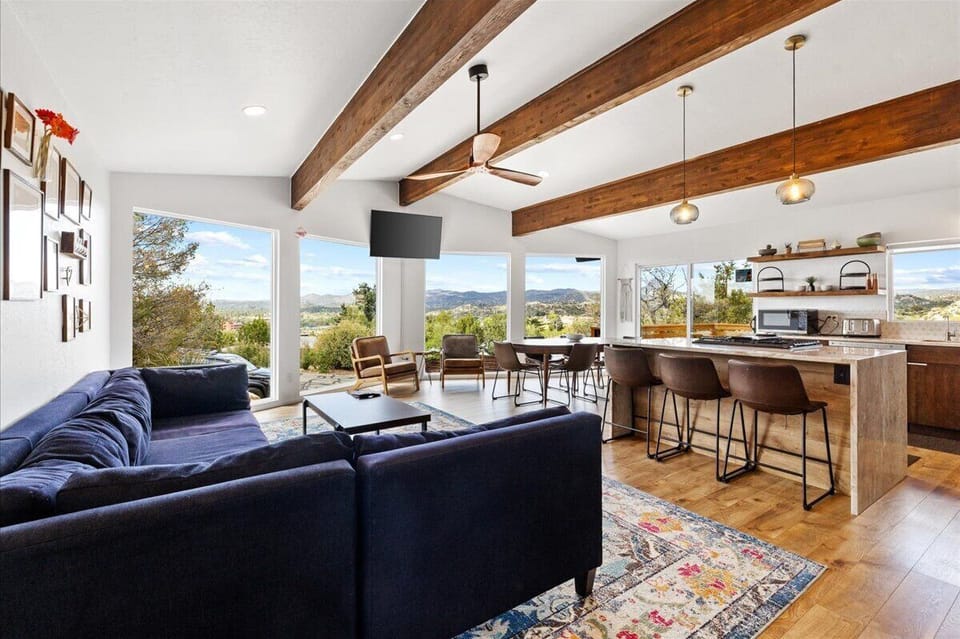 - Bright living room with open layout and stunning view windows - Large navy sectional and cozy seating for family relaxation - Wood beams and warm flooring create a welcoming gathering space coolvibe