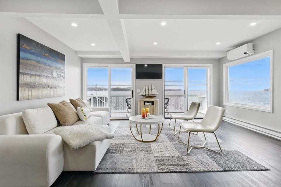 Modern lakeside living room with stunning waterfront views, plush seating, and natural light pouring through sliding glass doors—perfect for relaxing by the lake. 🌅🛋️☕