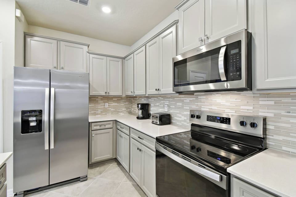 Step into a beautifully designed kitchen featuring sleek stainless steel appliances and elegant white cabinetry. The subtle stone backsplash adds a touch of sophistication, making it an ideal spot for culinary adventures.