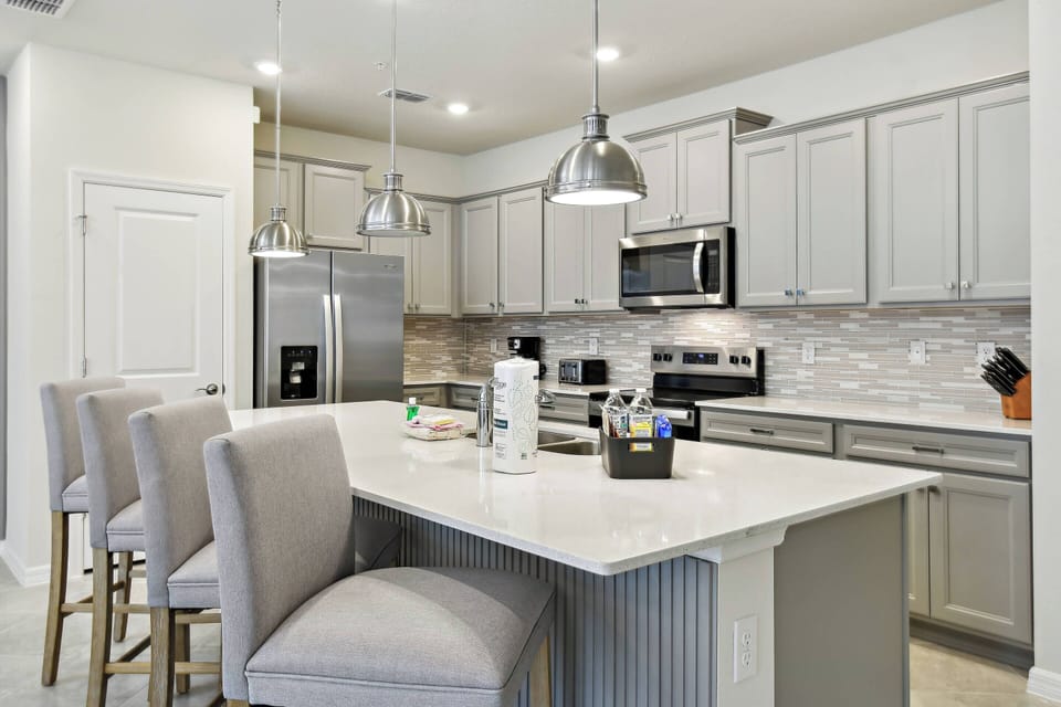 This stylish kitchen boasts sleek gray cabinetry and a stunning marble island with comfortable bar seating, ideal for casual meals or morning coffee, while polished stainless steel appliances enhance its contemporary charm.