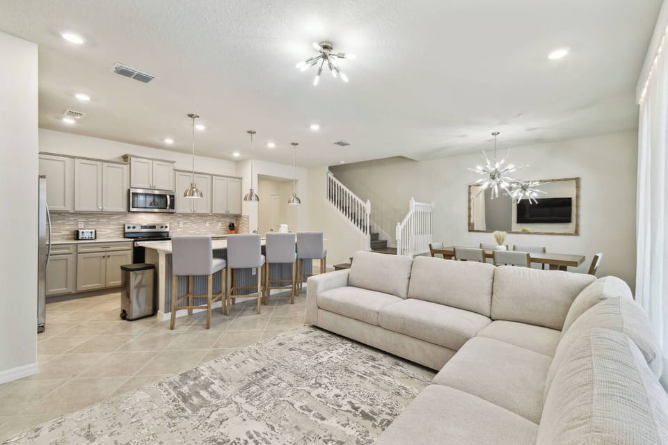 This inviting living space features a cozy light-colored sectional sofa and a chic area rug, flowing into a modern kitchen with sleek cabinetry and stylish lighting, creating the perfect setting for relaxation and gatherings.