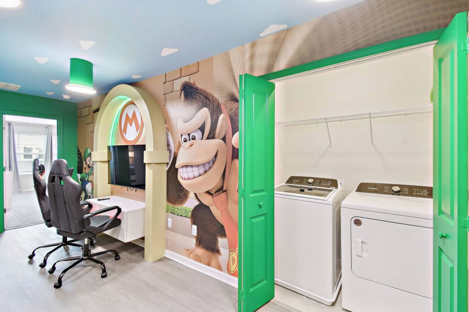 Discover a vibrant gaming nook with playful decor, a bold mural, and sleek gaming chairs against a cheerful green backdrop. The convenient laundry area blends effortlessly, ensuring your comfort while you enjoy the fun.