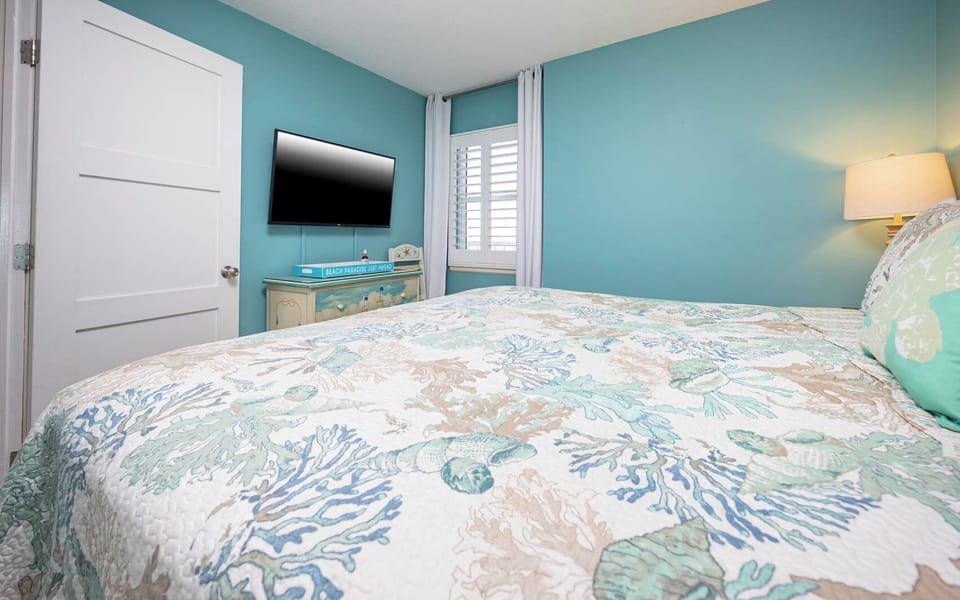 This cozy bedroom features a colorful coral-patterned quilt, a mounted TV, and a cheerful beach-themed decor