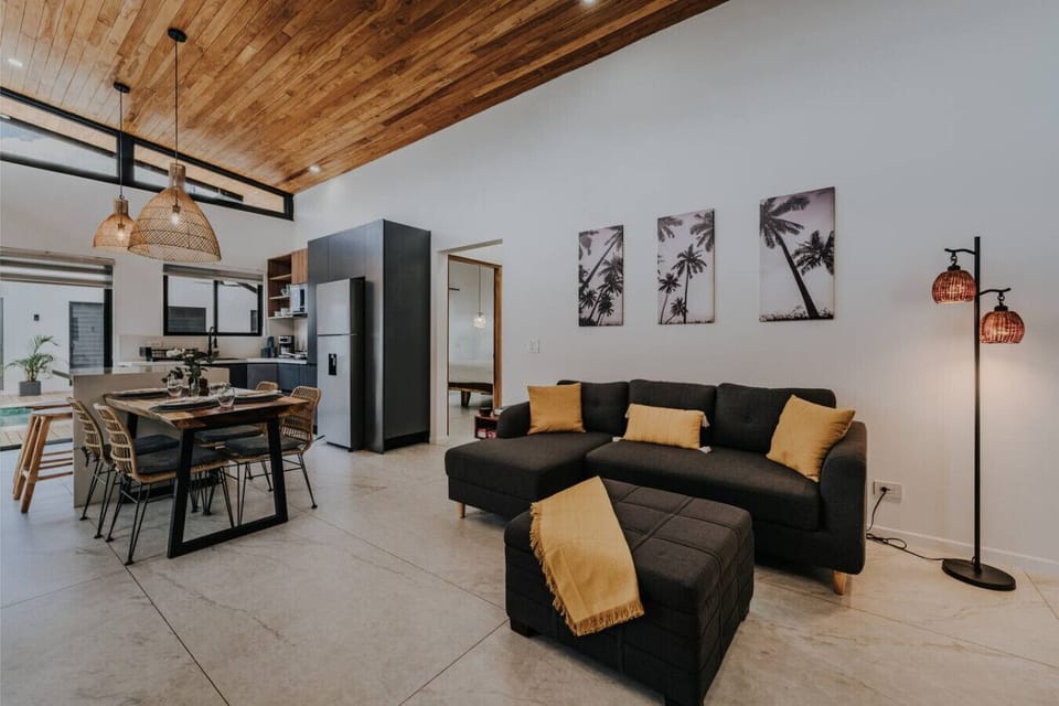 Bright, modern open-concept living flows seamlessly into a stunning kitchen and dining area. A cozy pull-out sofa, elegant bar counter, and rich wood ceiling details add warmth and style to this inviting, light-filled space.