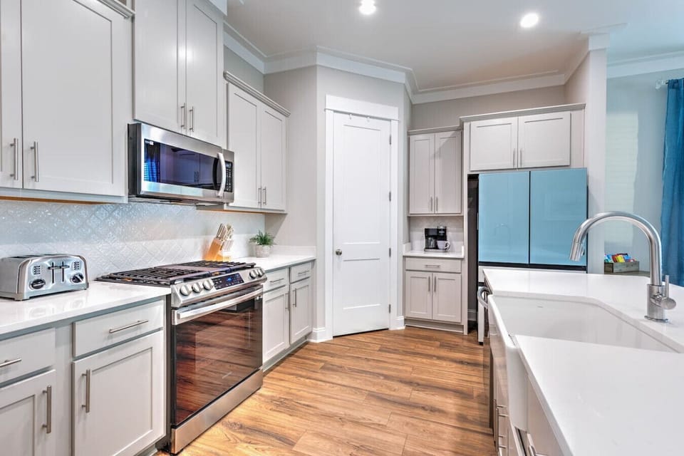 This kitchen has all the bells and whistles you`d actually want to use—think sleek white cabinetry, a proper gas range, and that huge island perfect for gathering while someone`s cooking up something good.
