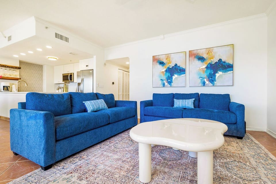 Sink into plush blue sofas in your spacious living area, where coastal artwork and modern comfort create the perfect retreat for relaxation and stunning sunsets.