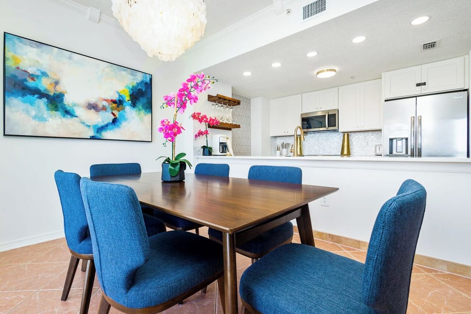 Gather around your elegant dining table where vibrant blue chairs invite memorable meals beneath a stunning chandelier.