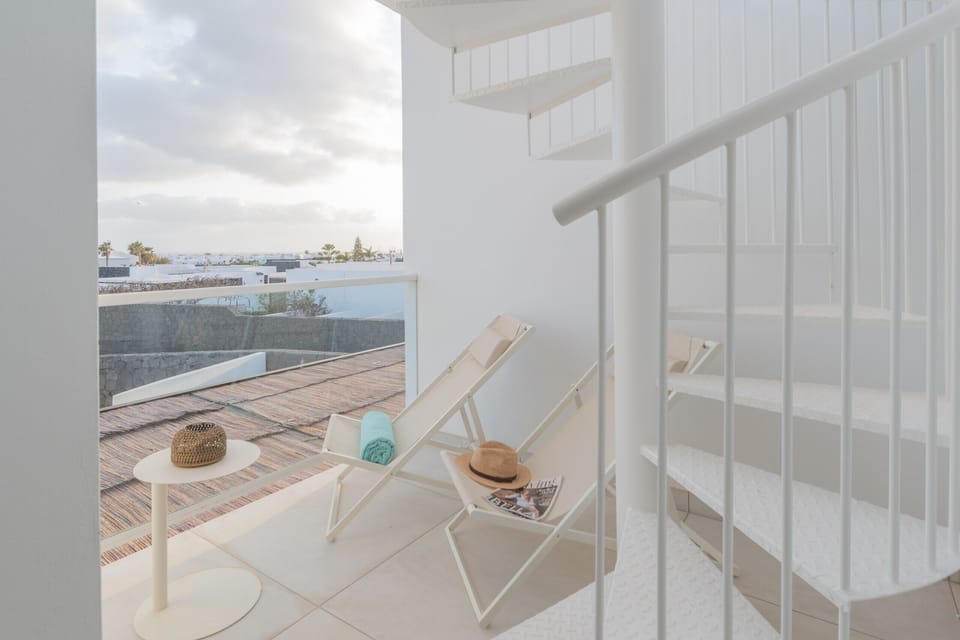Bright minimalist balcony featuring lounge chairs for relaxing and a stylish white spiral staircase.