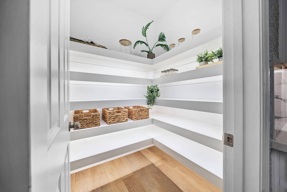 Step into this thoughtfully designed pantry, where sleek white shelving contrasts beautifully with warm wooden flooring. The subtle greenery adds a touch of freshness, making organizing your stay a delightful experience.