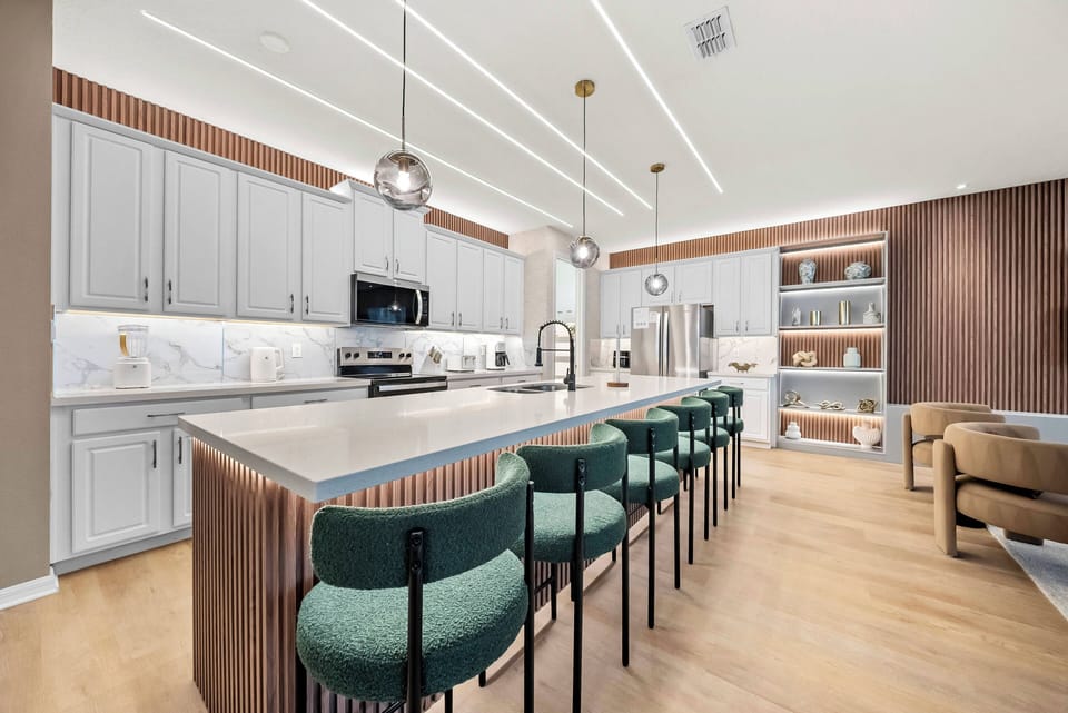 Enjoy delicious meals in our beautiful kitchen with sleek white cabinetry and warm wood accents. The spacious island with stylish green bar stools invites gathering, enhanced by modern lighting and elegant marble countertops.
