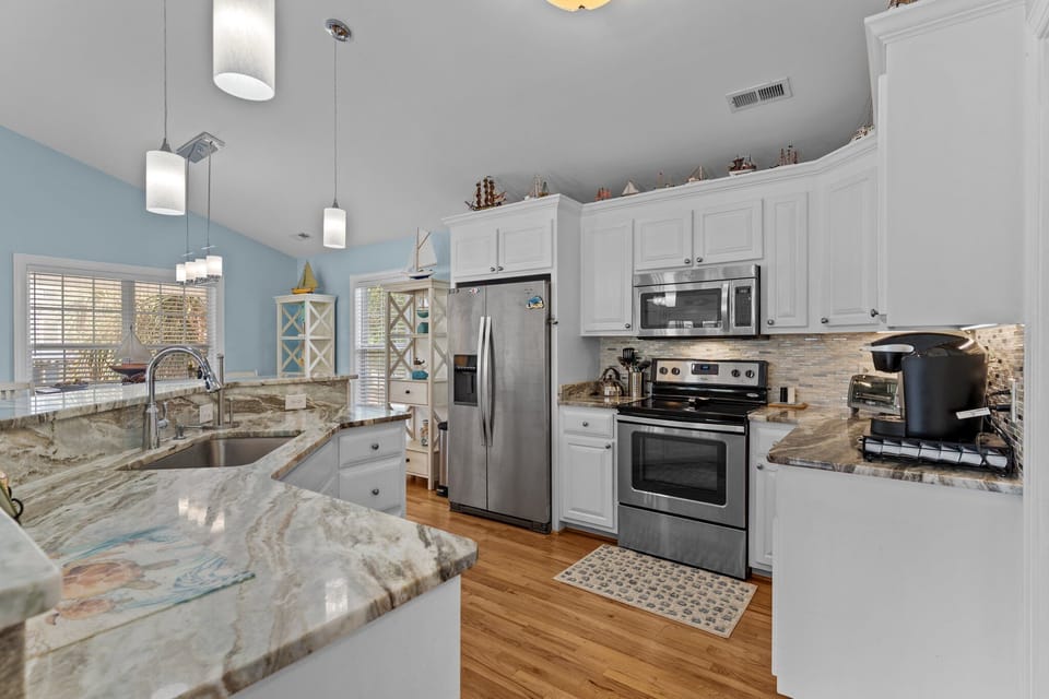 Bright kitchen with granite countertops, white cabinetry, stainless steel appliances, bar seating, and open layout flowing into dining and living areas.