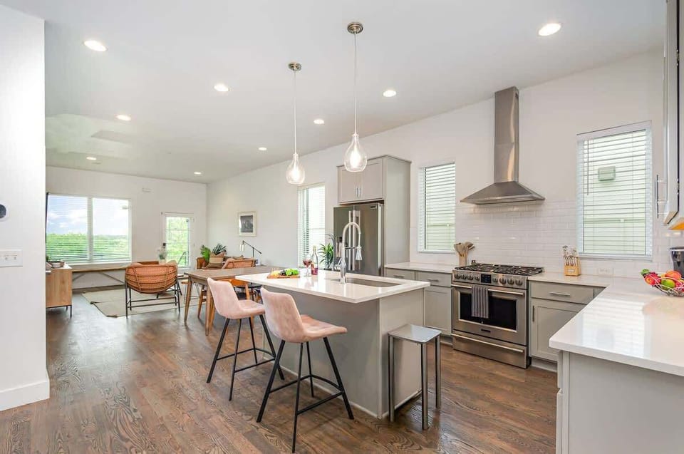 Bright open-concept kitchen featuring a quartz-topped island with bar seating, stainless steel appliances, and abundant natural light streaming through the windows.