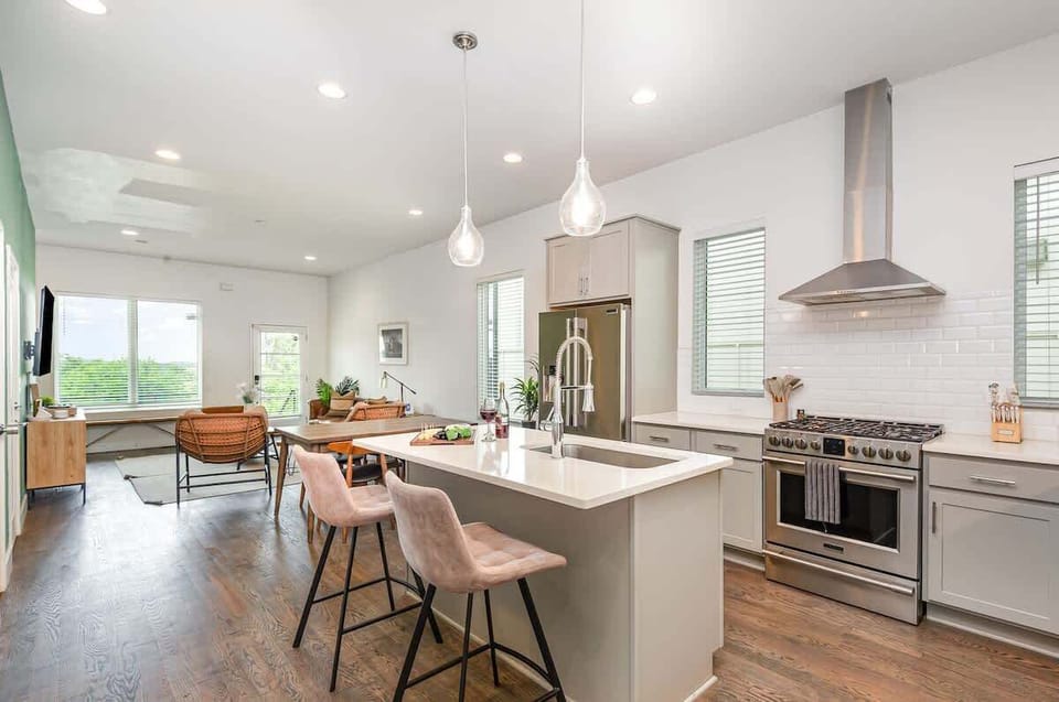 Bright open-concept kitchen featuring a quartz-topped island with bar seating, stainless steel appliances, and abundant natural light streaming through the windows.