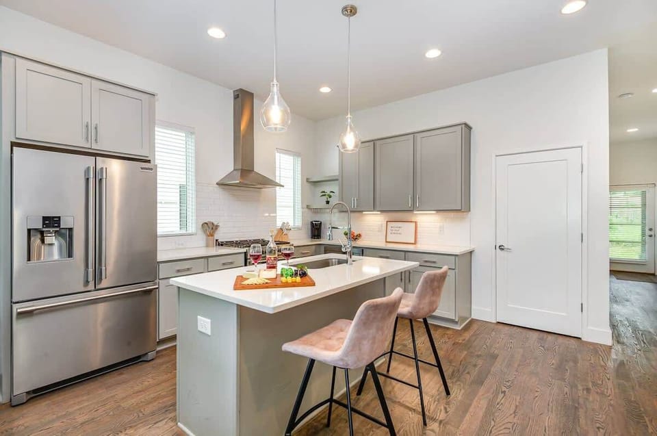 Bright open-concept kitchen featuring a quartz-topped island with bar seating, stainless steel appliances, and abundant natural light streaming through the windows.