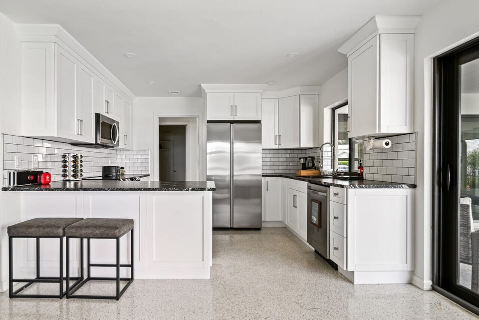 Modern kitchen boasts sleek white cabinetry, stainless steel appliances, and a breakfast bar, creating a stylish and functional space.

