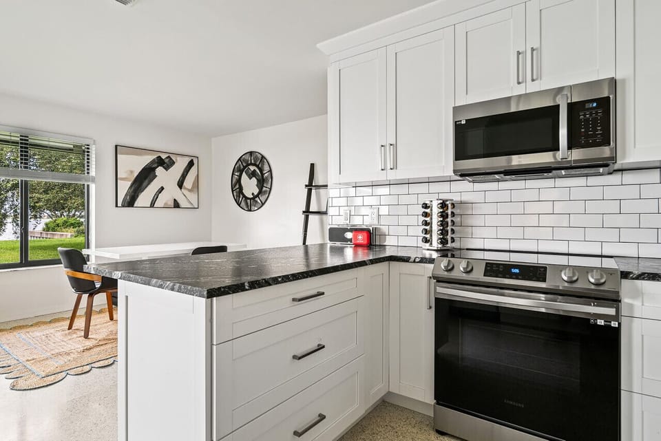 Modern kitchen boasts white cabinetry, stainless steel appliances, and a breakfast bar, offering a bright and functional space.
