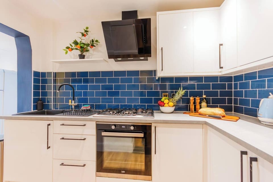 Fully equipped kitchen with sleek white cabinets, blue tiles, and a coffee machine, opening to the garden — great for cooking or gathering.