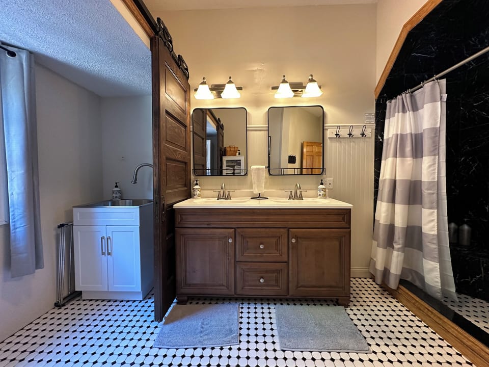 Main level bathroom with large shower, utility sink, and stacked laundry unit.