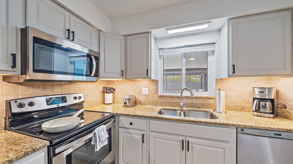 This gourmet kitchen is equipped with everything you need, including a full-sized stove, microwave, dishwasher, coffee maker, and granite counters, all overlooking the tranquil private pool area.