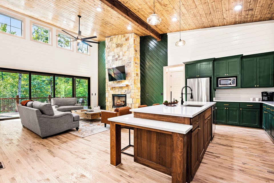 Designed for connection — gather around the kitchen island or curl up by the stone fireplace in this spacious open-concept living area with soaring ceilings and woodland views.