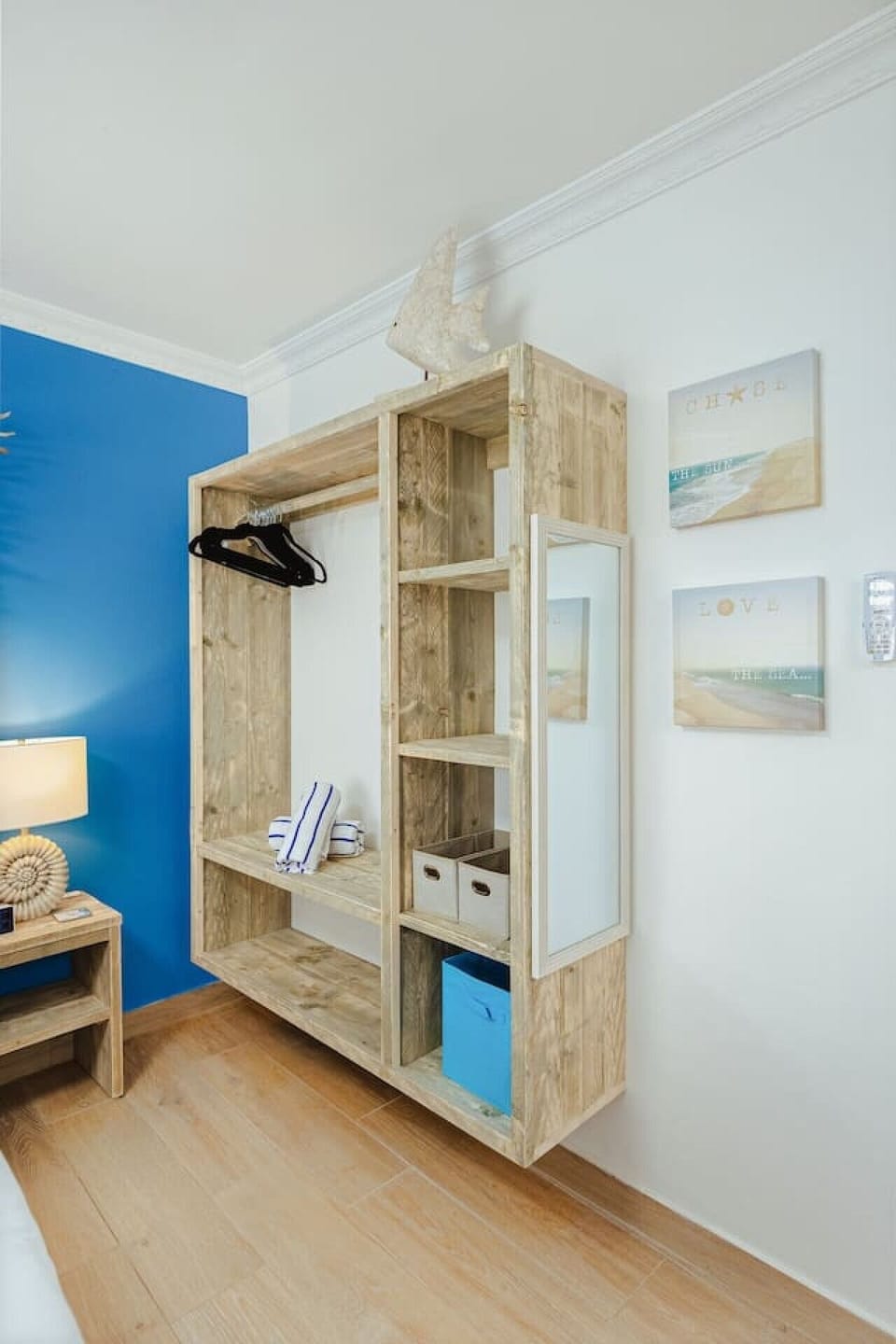 Close-up room corner detail showcasing a wall-mounted floating wooden wardrobe shelf with integrated storage baskets and an accent mirror.