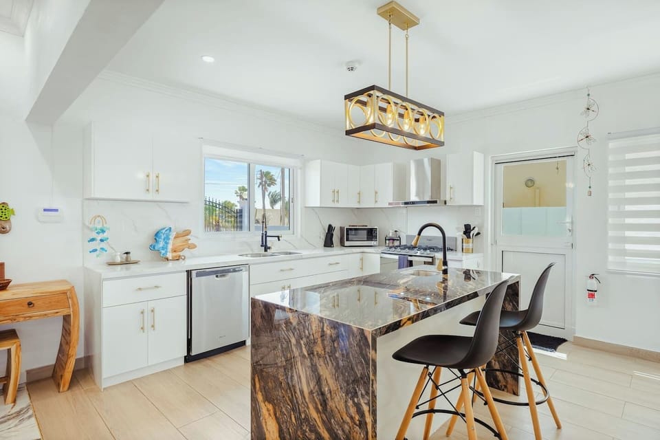 A wide view of the kitchen showcasing refrigerator, coffee maker, toaster, face to face sinks, ample cabinet storage, microwave, stove, oven and bar stools, all set in a cool ambient atmosphere for a perfect blend of functionality and modern design.
