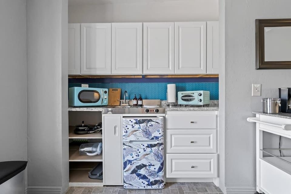 Whip up quick meals or morning coffee in this cheerful kitchenette, featuring charming retro-style appliances, a fun tropical mini fridge, and all the essentials.