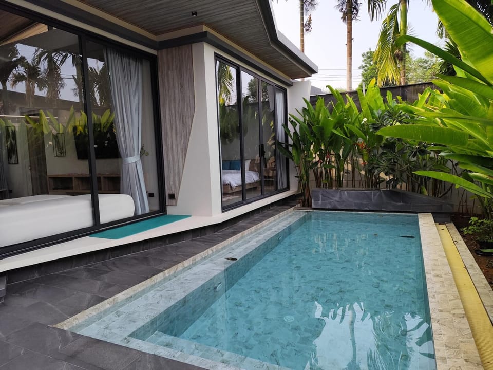 Aileen Villa’s exterior blends modern elegance with tropical charm—featuring a sleek private pool, sun loungers, lush garden, and shaded terrace. Surrounded by greenery and high walls, it offers privacy, relaxation, and a true Phuket retreat vibe.