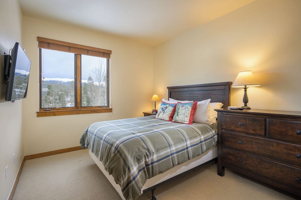 - Guest bedroom with soft plaid bedding and wide window views for natural light   - Warm wooden furniture adds rustic style to this inviting mountain retreat   - Peaceful atmosphere makes it an ideal room for rest after outdoor adventures