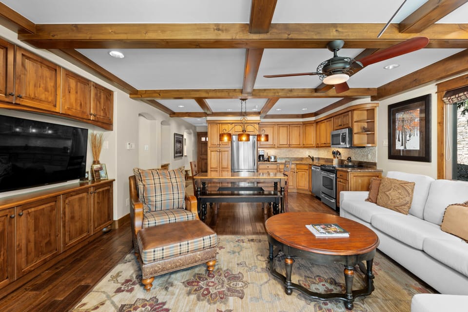 Inviting open-concept living space featuring a modern kitchen flowing seamlessly into a cozy living area with a sectional sofa, stone fireplace, and large windows that open to a wrap around patio.