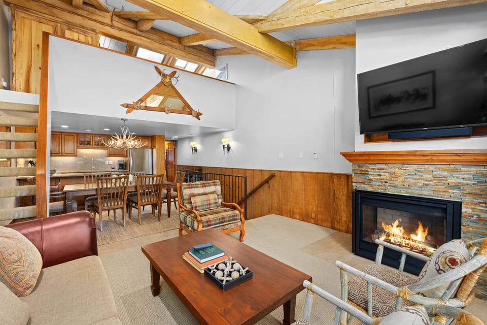 Inviting open-concept living space featuring a modern kitchen flowing seamlessly into a cozy living area with a sectional sofa, stone fireplace, and large windows that open to a balcony.