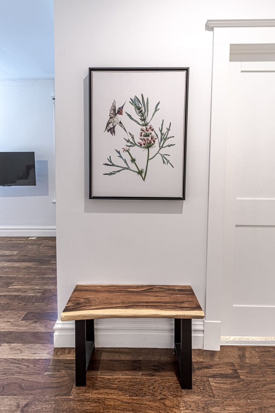 Bright Hallway Nook: Transition seamlessly between rooms in this clean, modern hallway featuring rich wood-look flooring, a solid wood bench, and elegant framed botanical art. Offering direct access to the adjacent bedrooms and living spaces, this welcomi