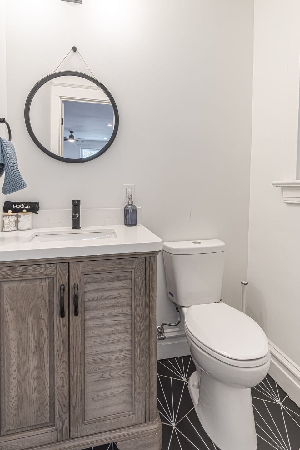 Modern Powder Room Vanity: Freshen up in this stylish half bath featuring a rustic wooden vanity, sleek white quartz countertop, integrated sink, and modern black faucet. Complete with a wall-mounted round mirror, luxury hand soap, and plush makeup towels