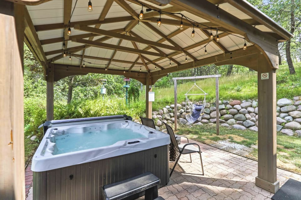 Soak your cares away under ambient bistro lights in this private outdoor retreat. Enjoy a soothing session in the hot tub or sway gently in the hammock swing surrounded by lush greenery and peaceful woodland views.