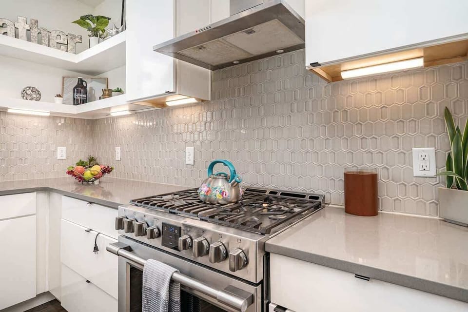 Bright open-concept kitchen featuring a quartz-topped island with bar seating, stainless steel appliances, and abundant natural light streaming through the windows. (1st Floor)