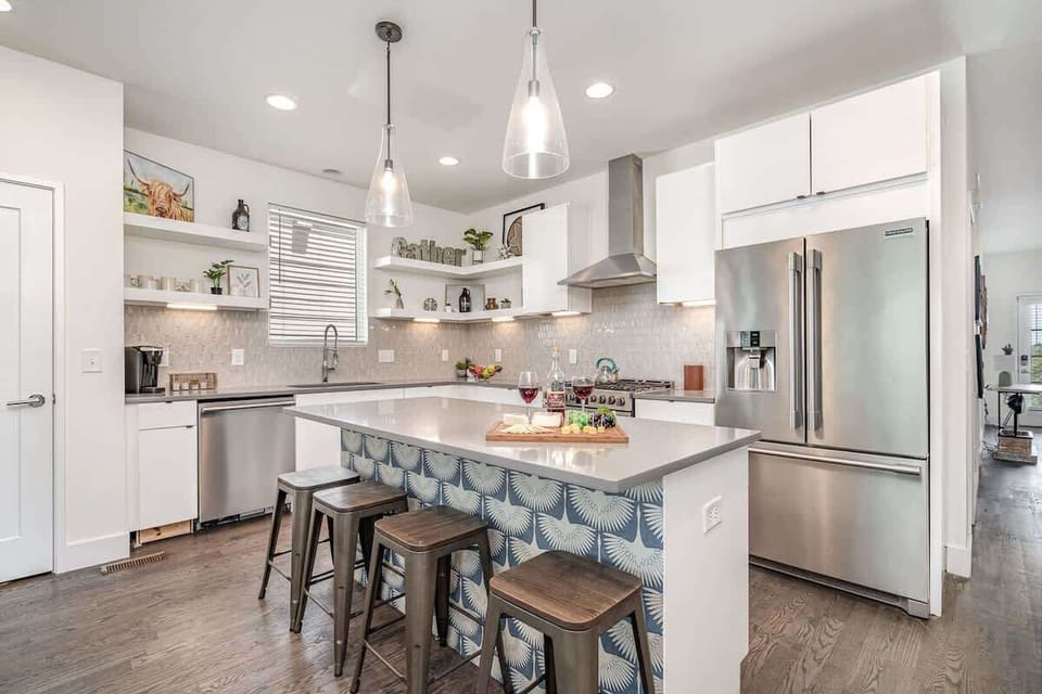 Bright open-concept kitchen featuring a quartz-topped island with bar seating, stainless steel appliances, and abundant natural light streaming through the windows. (1st Floor)